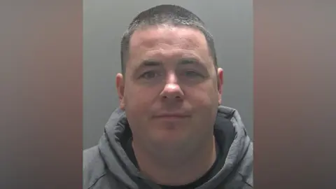 Hertfordshire Constabulary A police custody photo of David Lewis, who has short black hair and is wearing a grey hoodie.