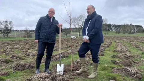 BBC First Minister John Swinney and Center Parcs chief executive Colin McKinlay plant a tree on the ground where a new holiday village will stand