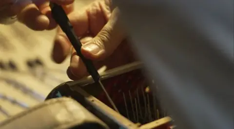 Hands using a tool work on an accordion