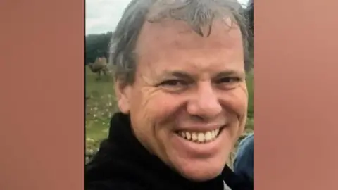 Caravan/Channel5 Donald McPherson, who is wearing a black turtleneck jumper, smiles while stood outside.