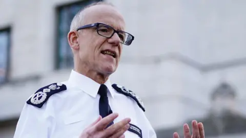 PA Media Sir Mark Rowley is wearing police uniform and glasses, he is gesturing with his hands as he speaks to reporters off camera