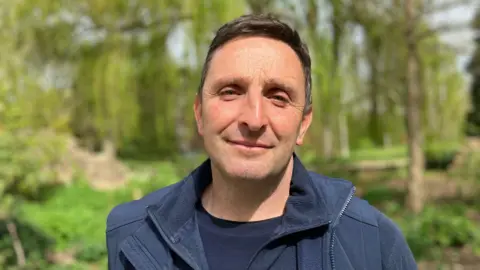Joe, a man with short brown hair, wearing a blue T-shirt and a blue jacket, smiling for camera. 