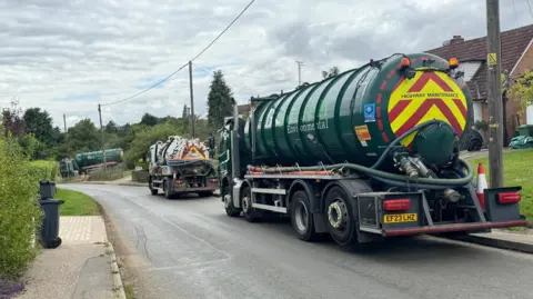 Elliot Deady/BBC Sewage tankers parked along a road in Great Easton