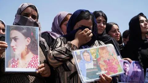 Getty Images Iraqi Yazidi women cry as they hold pictures of missing relatives during a ceremony in Chamishko camp, in the Kurdistan Region of Iraq, on the 10th anniversary of the IS Yazidi genocide (1 August 2014)