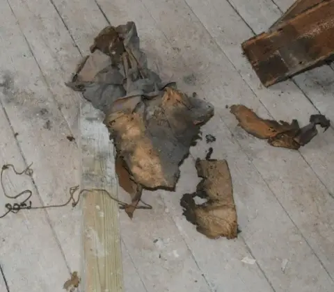 Durham Police Remains of an old brown dusty newspaper, next to which is a thin brown twine, all lying on the floorboards