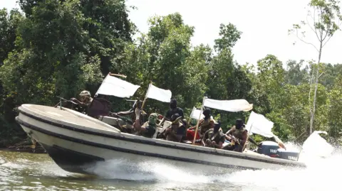 AFP via Getty Images Nigerian militants brandish theirs weapons in a speedboat with white flags flying in 2006