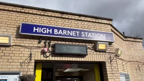 The entrance to High Barnet Station with a blue sign above the doorway on a brick building.