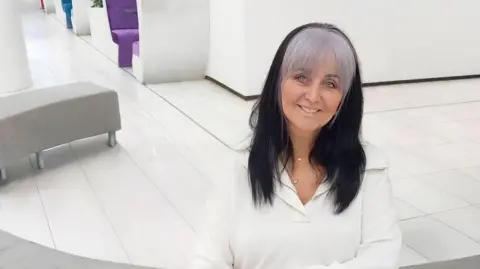 Slimming World A woman with black hair and a white fringe sat on a curved sofa