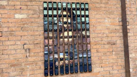 One hundred iPhones are pinned onto a brick wall and each screen shows a snippet of the Mona Lisa portrait