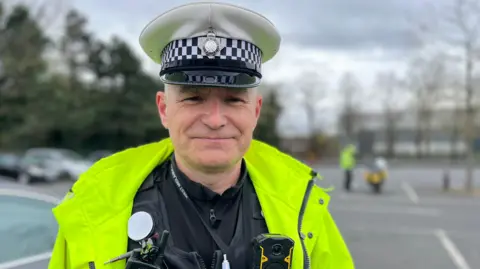 A male police officer wearing a white cap with a high-vis jacket and a West Midlands Police lanyard.