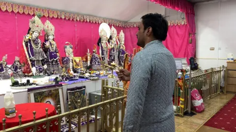 Hindu Temple Priest doing prays with a oil lit candle during a Puja. He is waving the oil candle in front of the Hindu statues.