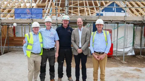 Duchy of Cornwall A Group of men stand in front of a part finished housing project , in the middle is HRH The Prince of Wales 