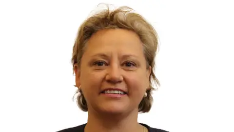 Rachel Kelsall, a woman wearing a black top, is pictured against a white background. She has short blonde hair and pearl-style earrings.