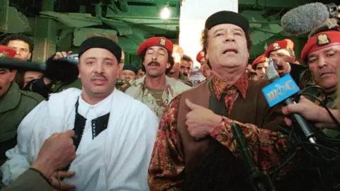 Getty Images Fhimah (left) speaks to the media with Libyan leader Muammar Gaddafi after arriving back in Tripoli the day after being acquitted in the Lockerbie bombing trial.