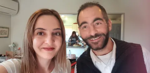 Family handout Aya al-Umari, wearing a white t-shirt, and her brother Hussein, in a sleeveless black jumper and white shirt, smile for the camera in a room where a kitchen can be seen in the background