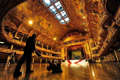AFP via Getty Images A maintenance engineer polishes the wooden floor during the annual cleaning of the ballroom in Blackpool Tower, the grand ceiling sparkling overhead.