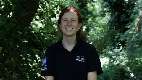 Facundo Arrizabalaga A woman with ginger hair smiles at the camera with green foliage behind her. 