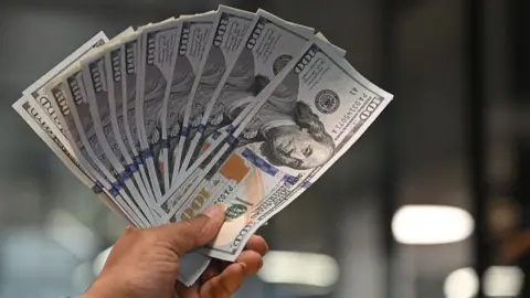 A worker holding US dollars banknotes poses for a photograph at a money exchange outlet in New Delhi on April 3, 2025. US President Donald Trump ignited a potentially ruinous global trade war on April 2 as he slapped 10 percent tariffs on imports from around the world and harsh extra levies on key trading partners. (Photo by Arun SANKAR / AFP) (Photo by ARUN SANKAR/AFP via Getty Images) INDIA-US-ECONOMY-TRADE-TARIFF