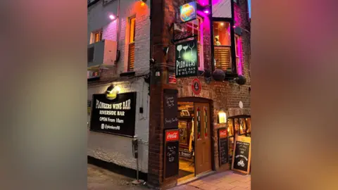 LDRS The exterior of Plonkers Wine Bar & Bistro is lit with purple and orange lights, highlighting its brick corner façade. 