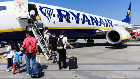 Passengers including children boarding a Ryanair aircraft on the steps at the fron of the plane on a sunny day with blue skies