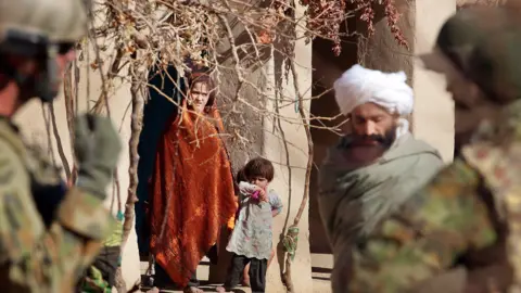 Getty Images/The Age A girl in an orange blanket and a young child look on as Australian forces patrol a town in Afghanistan