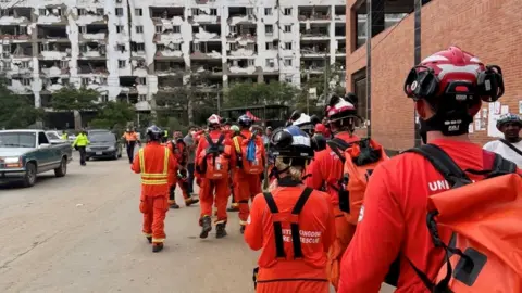 SFRS Firefighters in orange uniforms walking away from the camera in Venezuela.