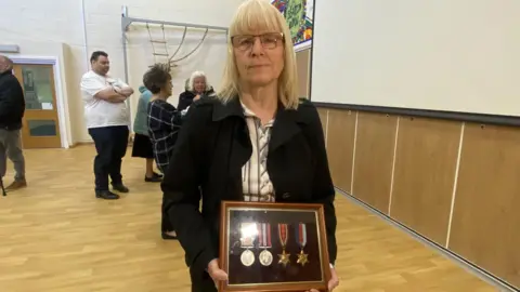 Donna Glennie, who has shoulder-length blonde hair, stands with her uncle's war medals