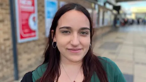 Shariqua Ahmed/BBC Adriana Fernandez is stood in the middle of the image looking at the camera. She had long brown hair and is wearing a green jacket. 
