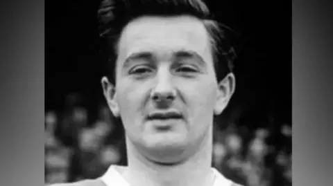 A black-and-white photo of Jeff Hall, who has dark hair and is clean shaven. He is prominent in the image and looking at the camera.