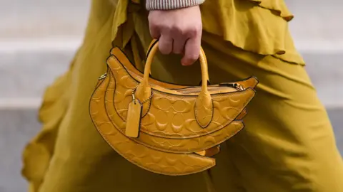 A yellow banana shaped leather bag with embossed logos from Coach.