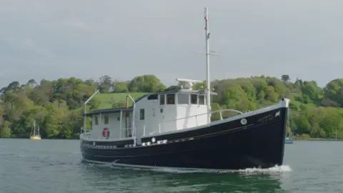 skyflicksmedia.com The Faithful, a blue hulled boat with a large white wheelhouse, pictured after a refit, sailing near Galmpton