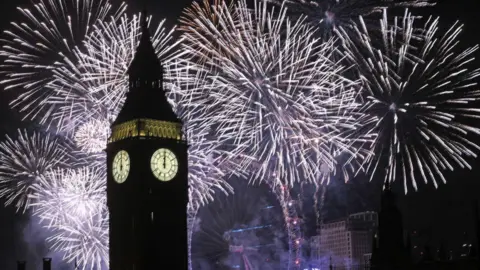 Fireworks explode in the sky behind the clock faces of Big Ben, with the London Eye in the background.  