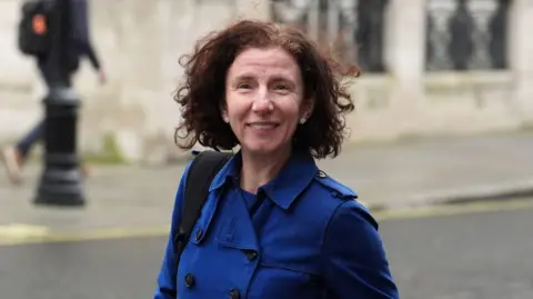 PA Media Anneliese Dodds has medium length dark hair and is wearing a blue mac rain coat.
