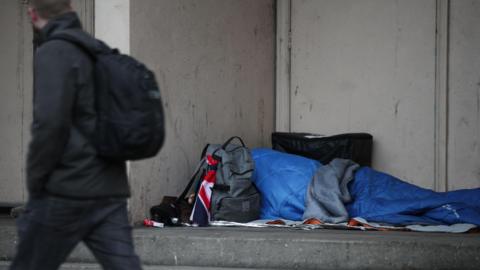 A person walking past a person sleeping rough and lying in a sleeping bag
