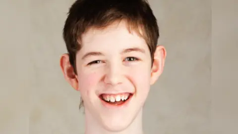 A teenage boy with short brown hair, smiling and looking directly at the camera
