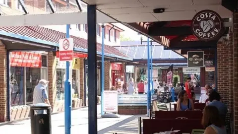 A general view of Thatcham town centre, with people walking through a shopping arcade and people sat outside.
