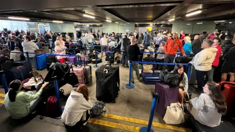 Reuters Passengers queue outside Terminal 1 after an overnight power cut led to disruptions and cancellations at Manchester Airport 
