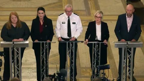 PA Media Justice Minister Naomi Long, deputy first Minister Emma Little-Pengelly, PSNI chief Constable Jon Boutcher, First Minister Michelle O'Neill and chair of the policing board Brenda Mullan speaking to the media at Parliament buildings at Stormont in Belfast