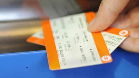 A hand takes two orange and yellow striped tickets from a silver slot in a blue ticket machine