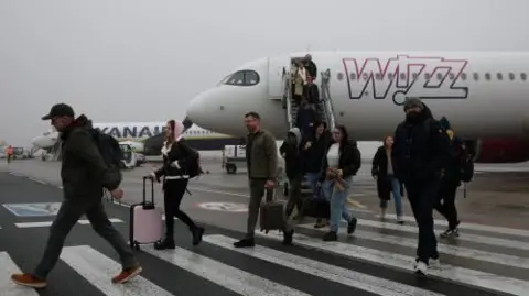 Reuters Passengers disembark from a Wizz Air plane, walking across the tarmac, with their carry on luggage 