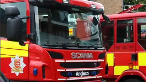 ECFRS Two red and yellow fire engines parked next to each other in a yard.