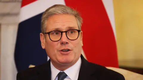 PA Media Sir Keir Starmer sitting on a chair in front of a Union Jack flag