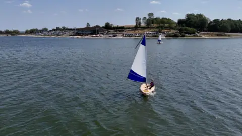 A sailing dinghy with a white and blue sail on a reservoir