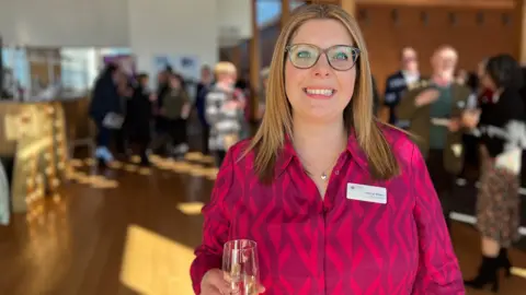 Jon Wright/BBC Hannah Bloom stands in front of a room full of people ready to make a toast.