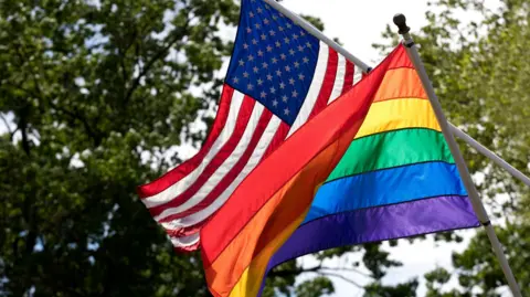 US and Pride flags fly side-by-side in a stock image