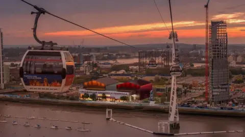 Troubadour A proposal image of a cable car going across the Thames towards the new Troubadour Theatre as the sun sets over the Greenwich Peninsula. 