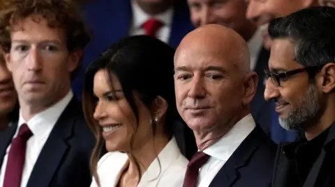 Appearing at the second inauguration of Donald Trump, from left to right: Mark Zuckerberg in a black suit, white dress shirt and red necktie; Lauren Sanchez, in a white suit; Jeff Bezos in a navy suit, white dress shirt and red neck tie; Sundar Pichai in an all black suit, shirt and neck tie.