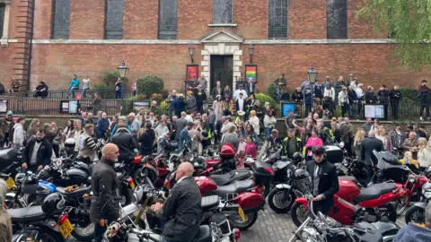BBC/Morgan Webb Motorbikes parked outside a building with crowds of people.