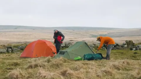 Two campers with an orange and green tent on an open grassland morland.