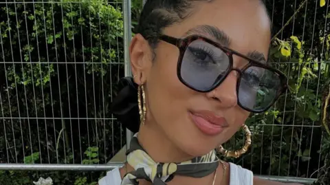 A woman is wearing large sunglasses and earrings, and is looking at the camera.